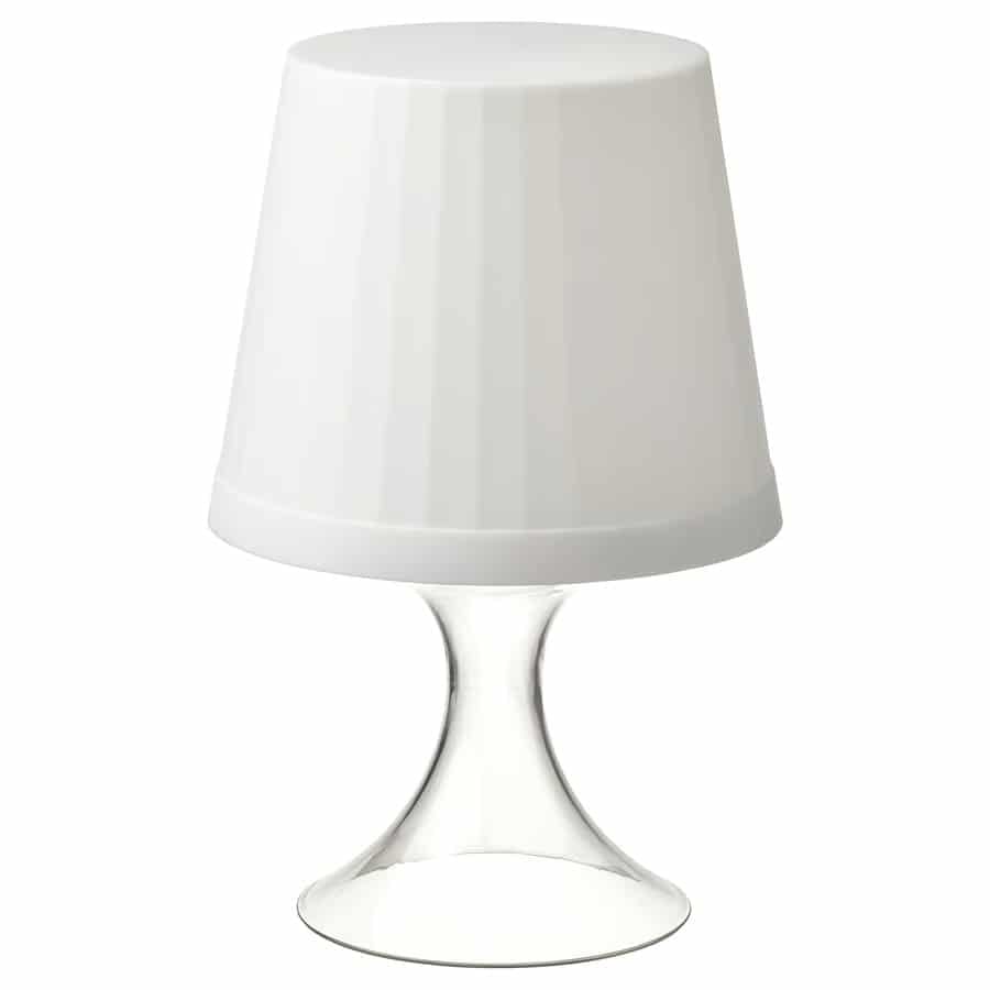 White lampshade on a clear glass pedestal table lamp against a white background.