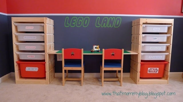Wooden toy storage shelves flank a small table with two red-and-blue chairs; LEGO LAND on the wall with a few LEGO bricks on the table.