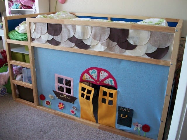 101_0262 - IKEA Hackers Child's bed with a blue fabric wall decorated by a yellow double door, pink window, and flower garden; scalloped gray and white cloud border along the top.