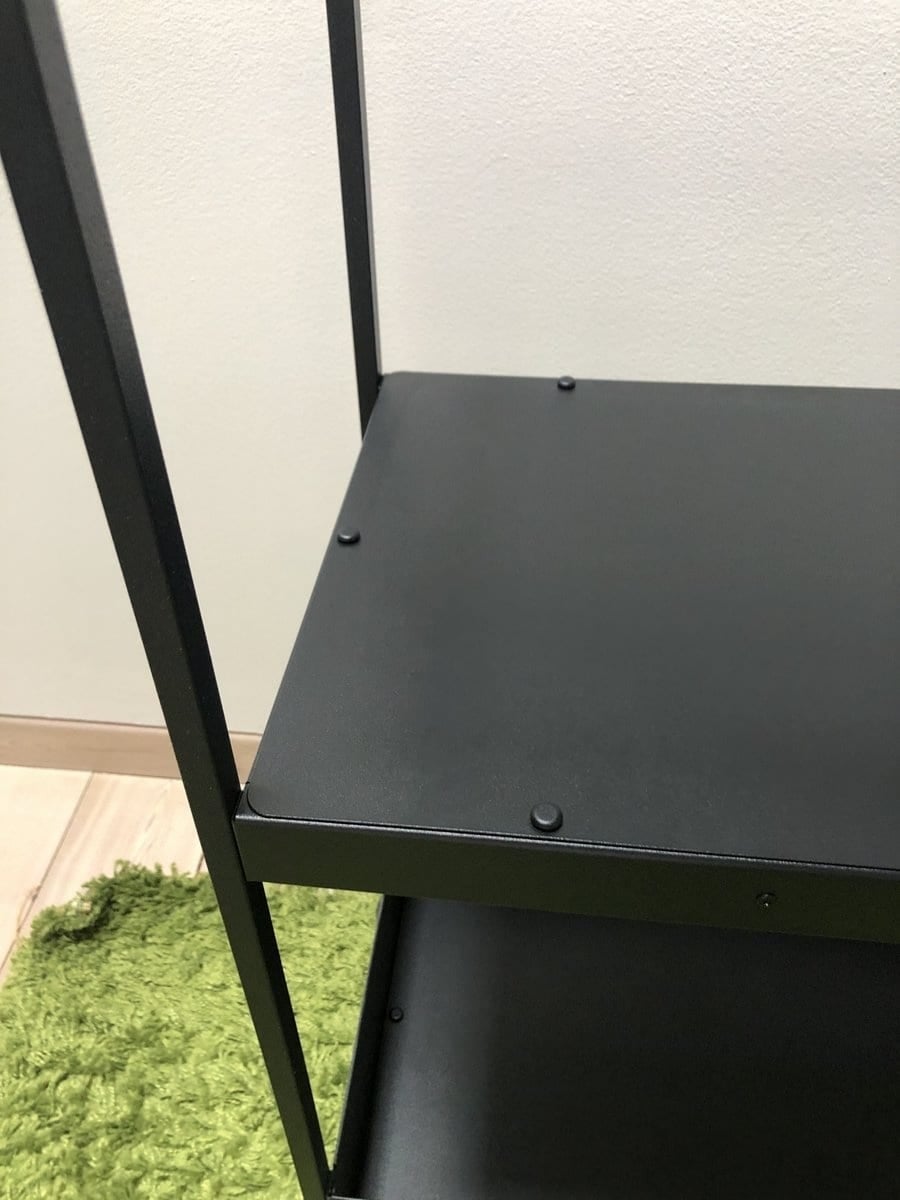 Close-up of a black metal shelving unit corner with screws on the top shelf