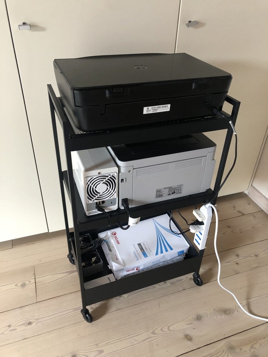 Metal rolling cart with two printers: a black top printer and a gray mid-sized printer, with cables and a power strip visible on the side.