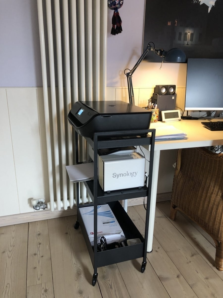 Printer on a black rolling cart with a Synology NAS box beneath, in a tidy home office next to a desk and monitor.