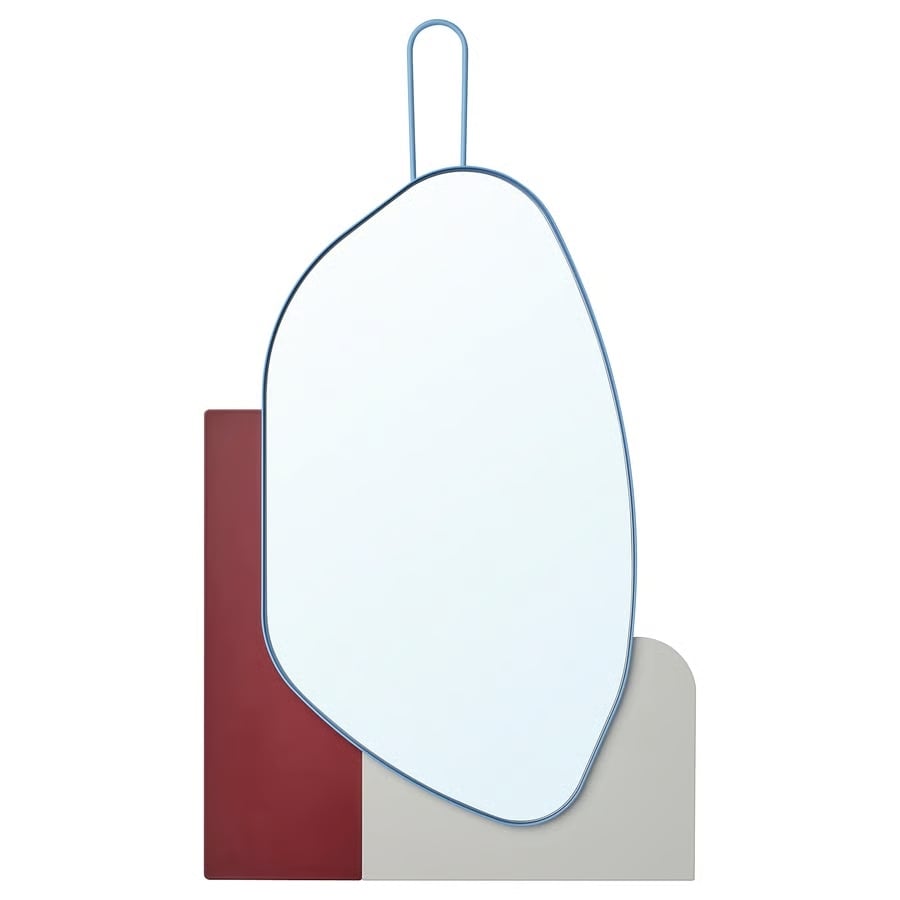Geometric wall mirror with an irregular oval, blue frame and hanging loop, mounted over red and beige rounded blocks.