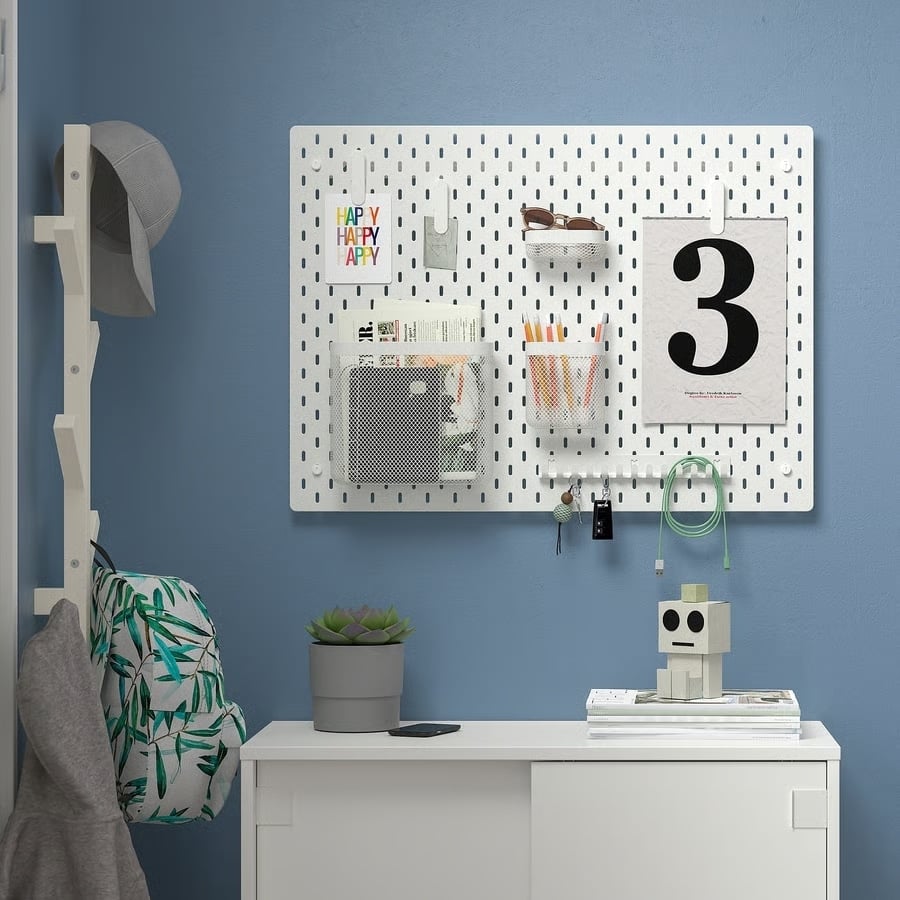 22 - IKEA Hackers White pegboard with storage pockets and a large calendar page showing the number 3, mounted on a blue wall above a white cabinet.