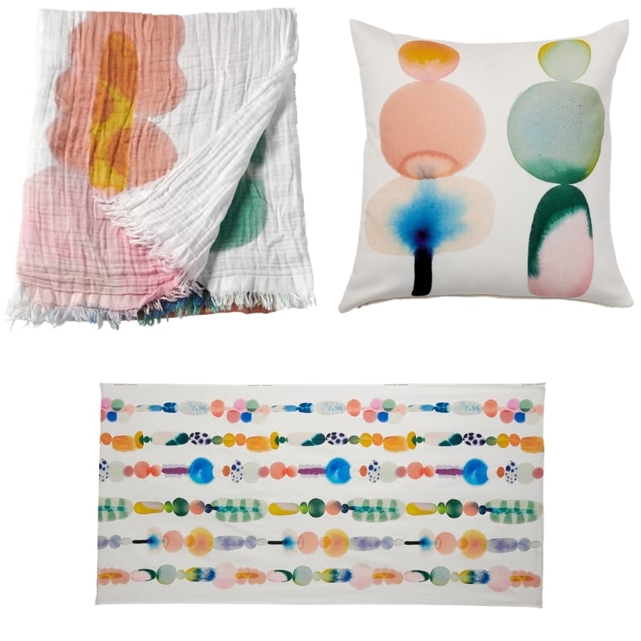 White woven throw blanket with pink, orange, and yellow watercolor shapes and fringed edges, folded at the corner