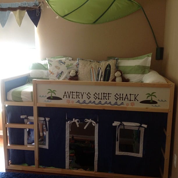 644042_3945475590283_1892519075_n-701169 - IKEA Hackers Loft bed for a child with a surf shack theme; sign reads 'Avery's Surf Shack' over a blue fabric play area beneath, with pillows and stuffed toys above.