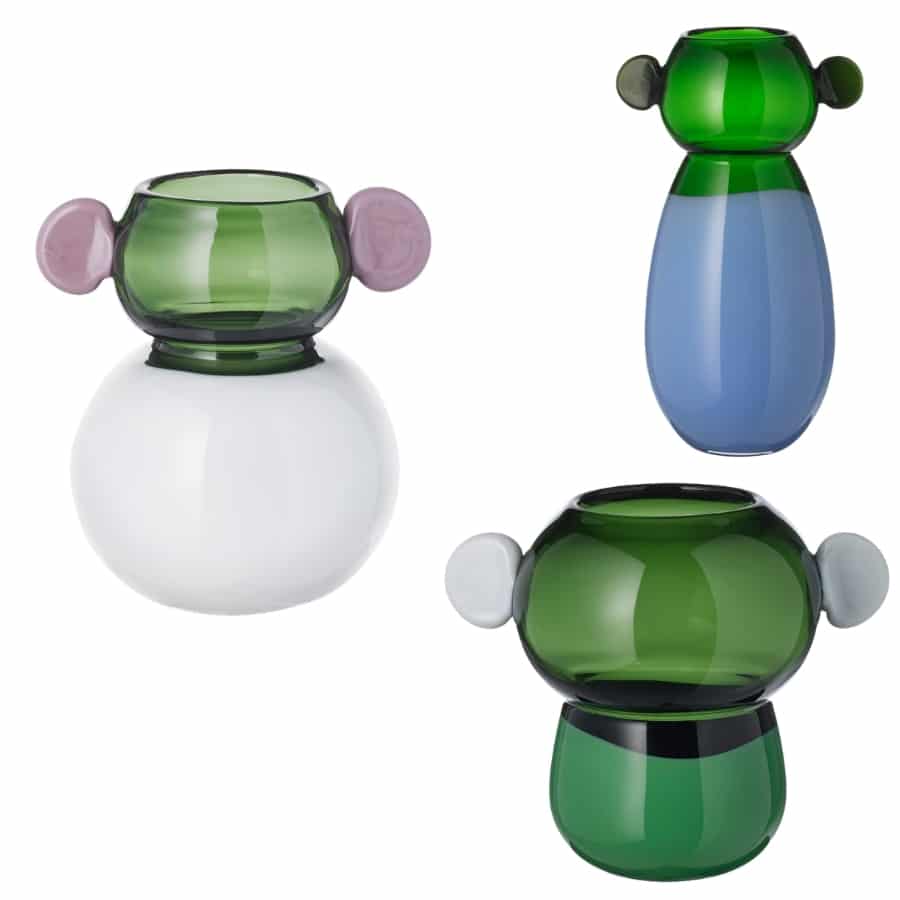 Three colorful glass vases with round bodies and small ear-shaped handles in green, white, and blue tones set against a white background