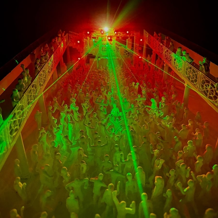 Mini rave table IKEA coffee table hack that has the scene of a crowded nightclub dance floor bathed in red and green lights with green laser beams, seen from above near the balcony railings.