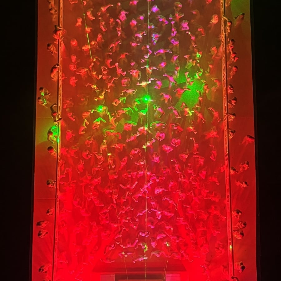 Overhead view of a crowded, red-lit space with many people along the glass walls and a few green light spots in the center.
