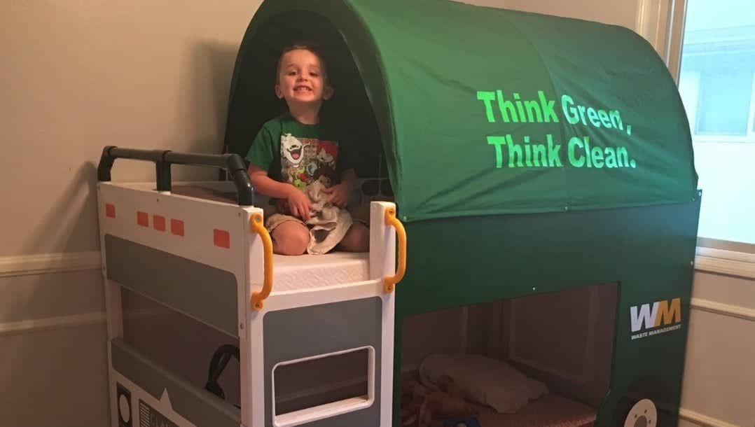 IKEA-KURA-trash-truck-bed-featured - IKEA Hackers Young child sits on top of a white and gray toy bus with yellow railings, under a green canopy that reads 'Think Green, Think Clean.'