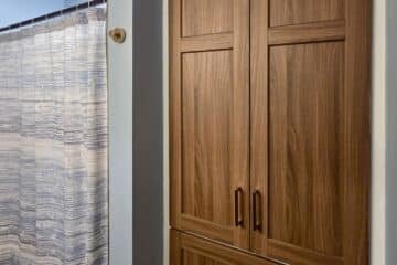 Wooden bathroom cabinets with tall doors and drawers next to a blue-walled shower area with a striped curtain.