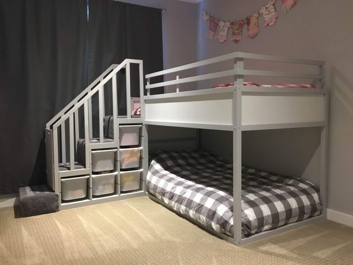 IMG_9763 - IKEA Hackers Gray children's bunk bed with stairs and built-in storage drawers, lower bunk with plaid gray-and-white bedding, purple rug nearby, garland on wall.