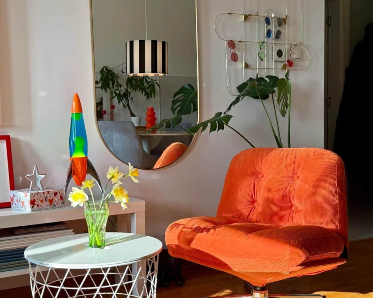 Orange upholstered lounge chair beside a white round coffee table with a glass vase of yellow flowers in a modern living room.