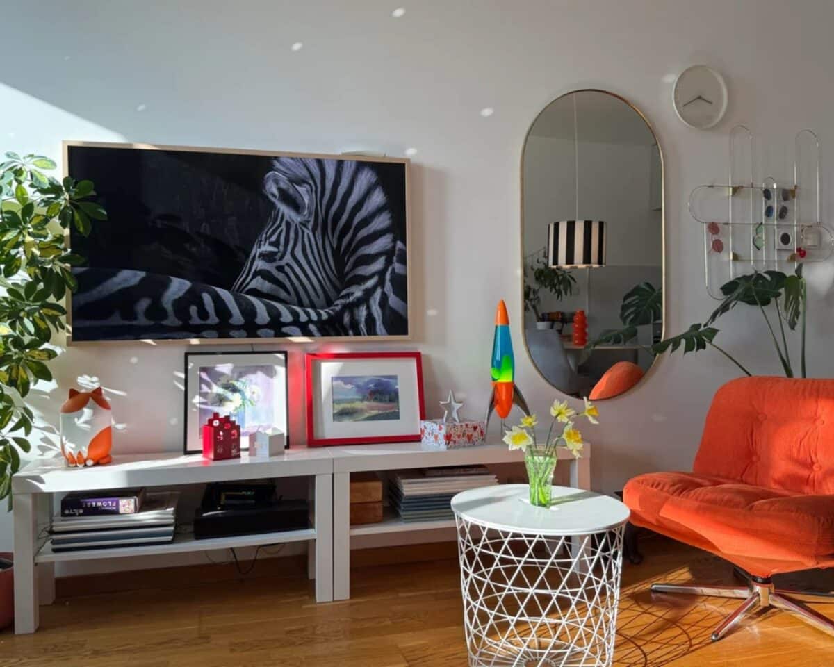 Living room with zebra artwork on a wall-mounted screen, an orange chair, plants, and a white coffee table.