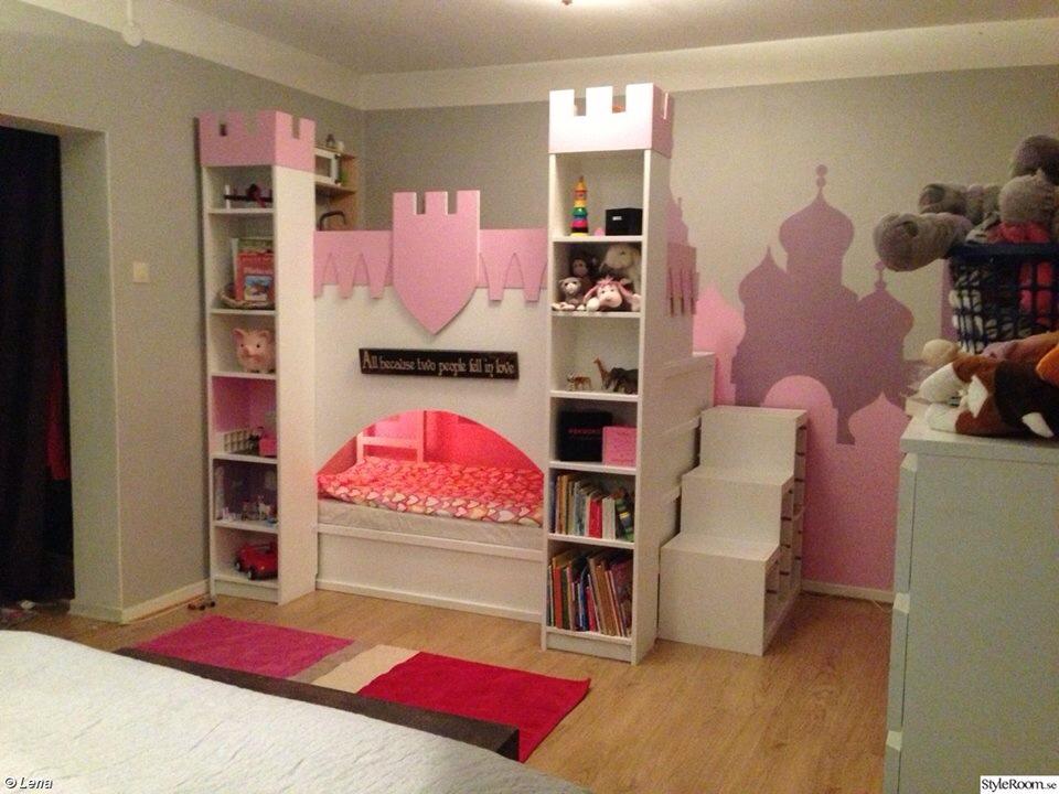 kuracastle5 - IKEA Hackers A pink and white castle-themed bunk bed with shelves and a small bed, in a kids’ bedroom with a pink mural and stuffed animals nearby.