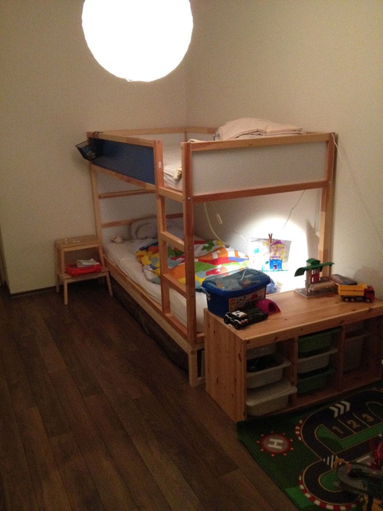 photo-767x1024 - IKEA Hackers Wooden bunk bed in a small child’s room, with colorful bedding, toy storage under the desk, and a play rug nearby.