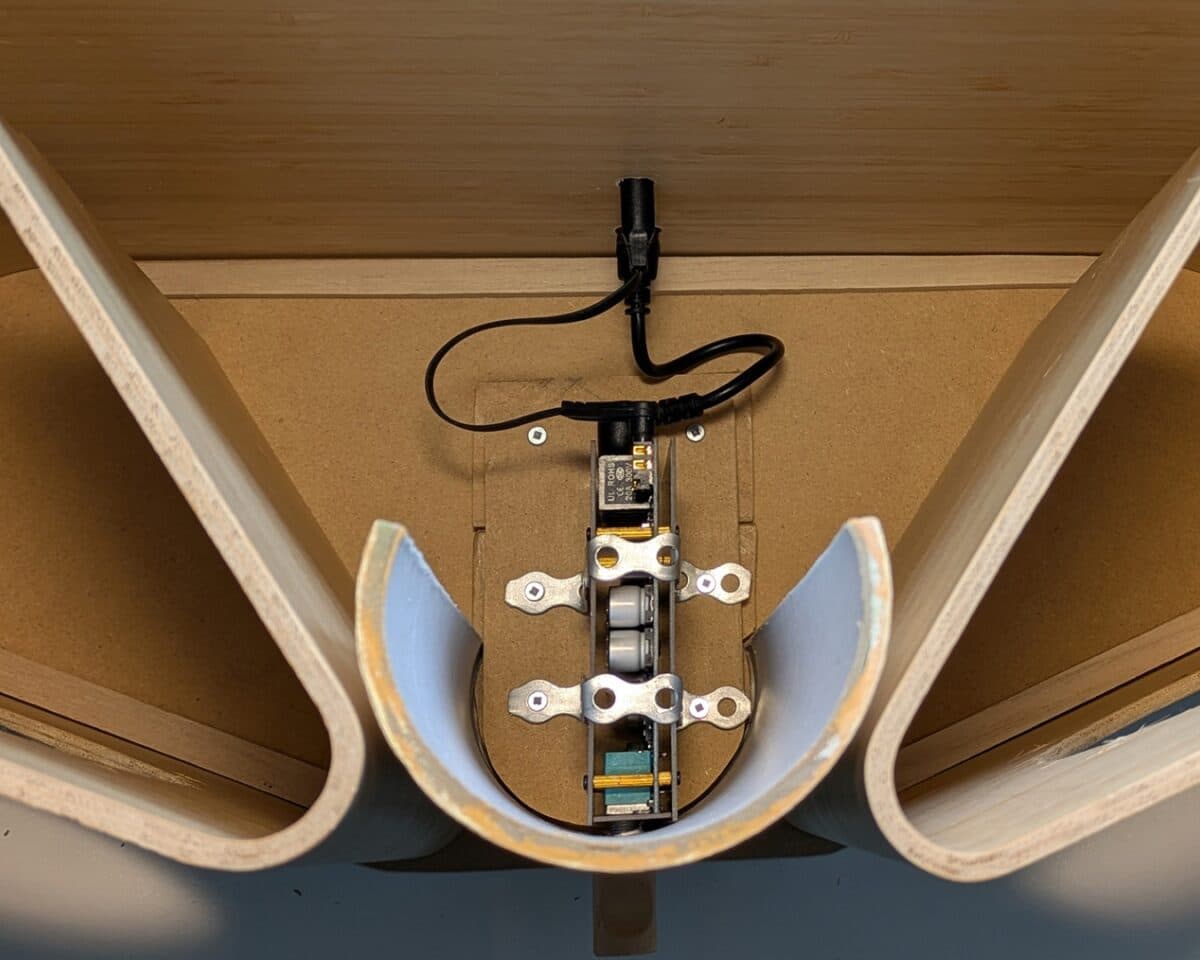 10 - IKEA Hackers Close-up of a small roller carriage mounted inside a U-shaped wooden channel, with metal brackets and a black power cable connected at the top center.