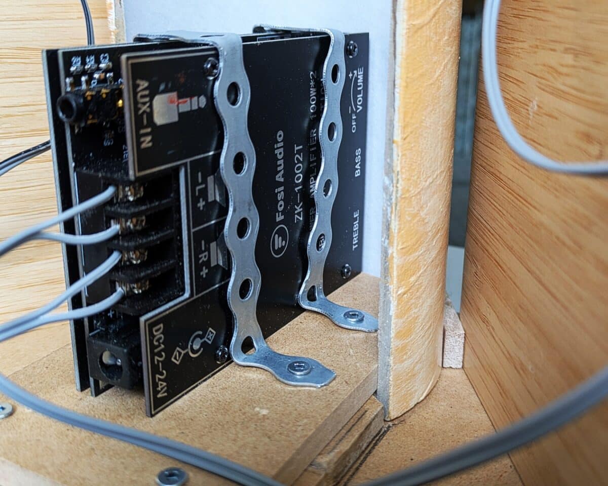 11 - IKEA Hackers Close-up of an audio amplifier/crossover module mounted inside a wooden speaker cabinet with terminal blocks and metal clamps.