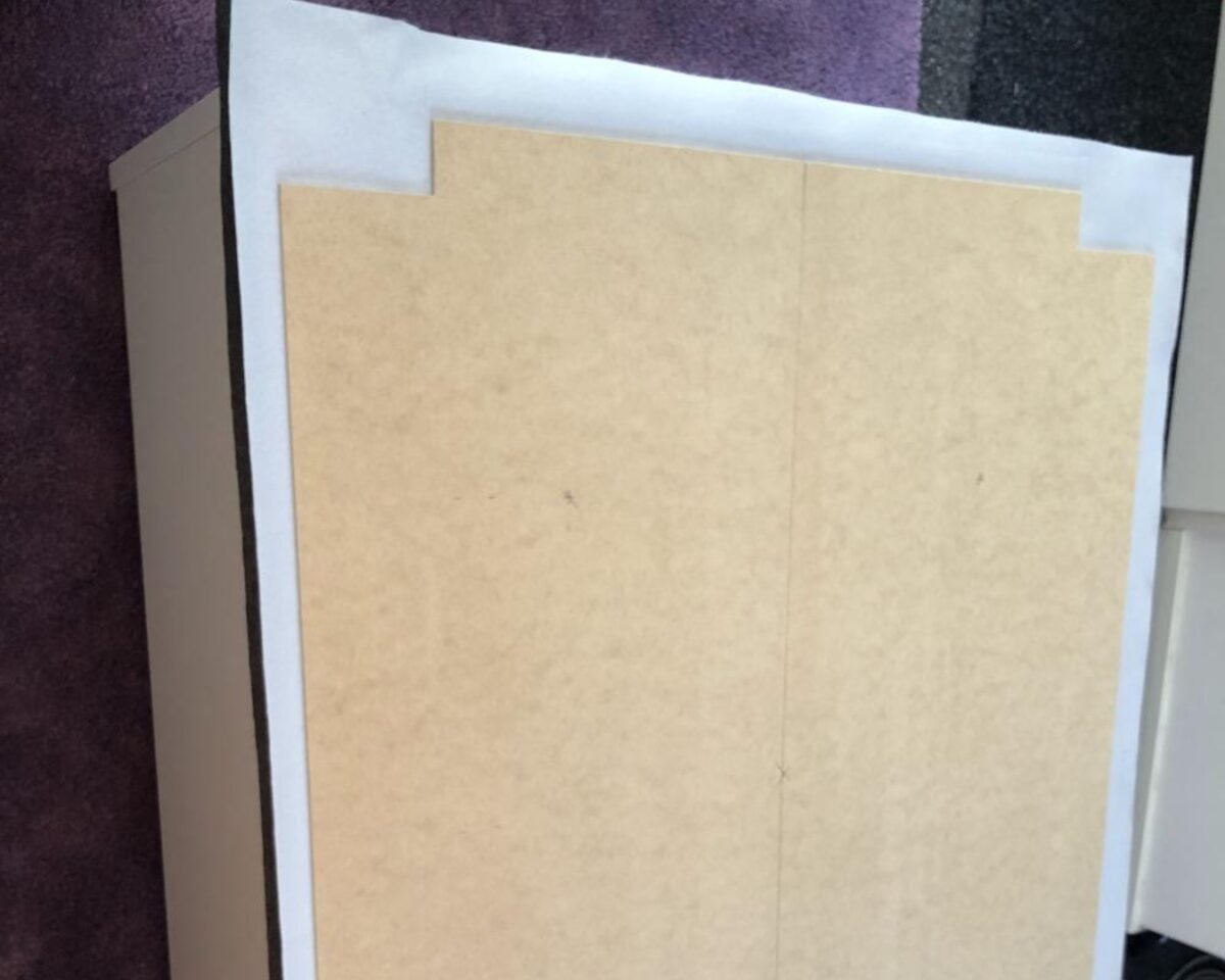 Two beige cardboard panels placed side by side on a white sheet, with small stepped notches at the top edges and a purple carpet floor in the background.