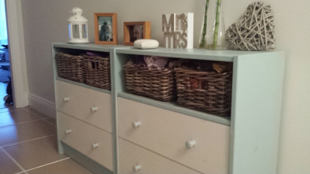 2014-07-14-214622 - IKEA Hackers Two light-blue dressers with open woven baskets on top and white knobs, decorated with frames, a lantern, and a heart sculpture.