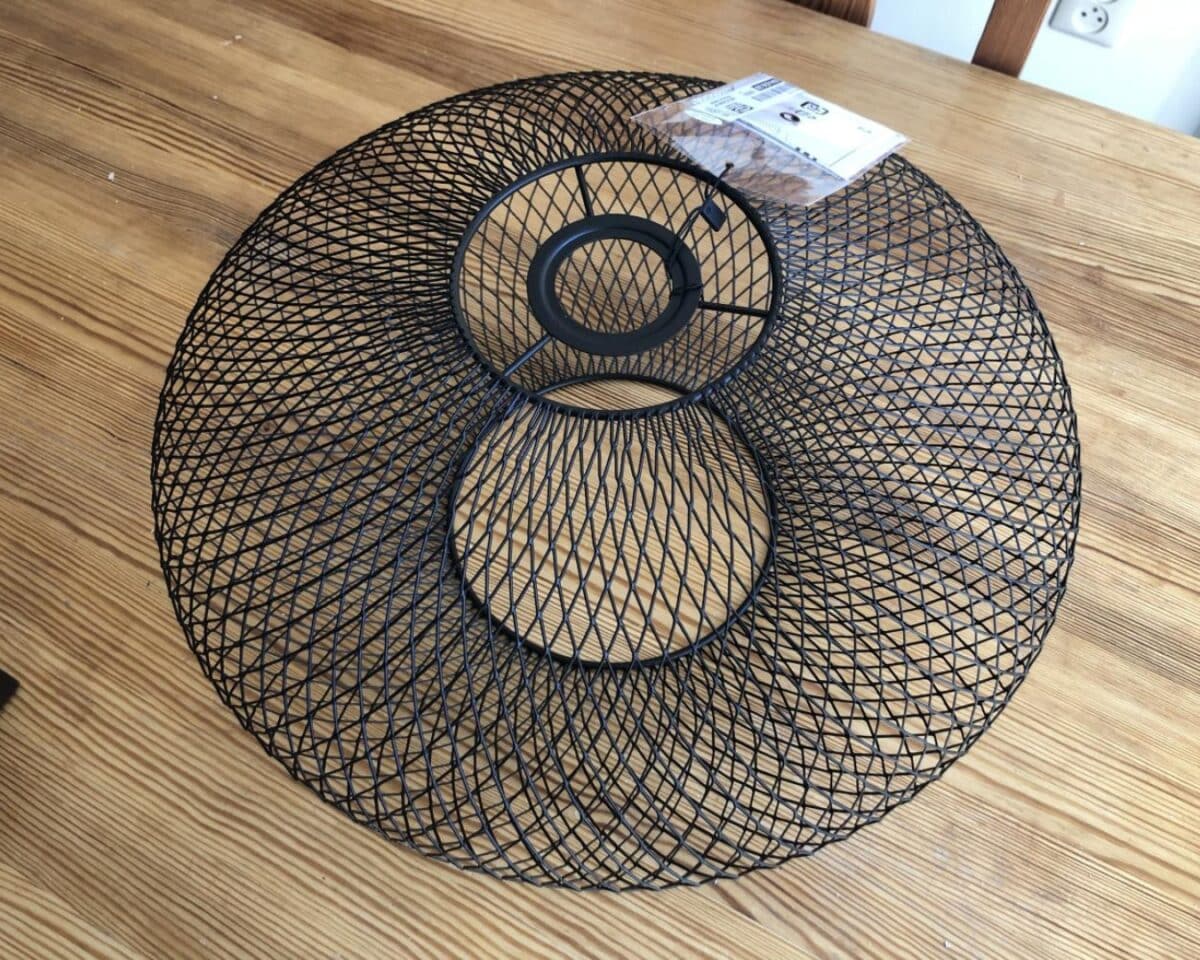 Black circular wire-mesh lamp shade with a central ring, lying on a wooden table.