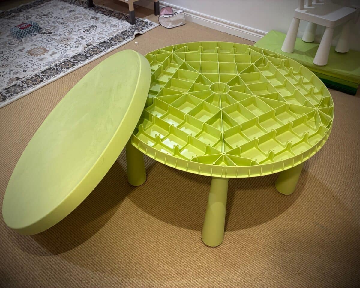 IKEA MAMMUT table. Lime-green round activity table with a grid-pattern top and a matching lid in a playroom.
