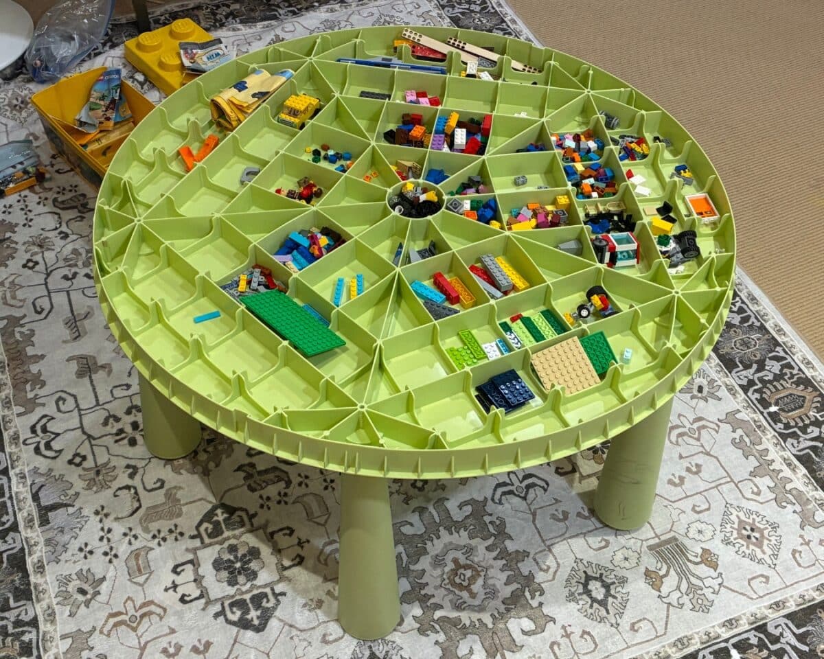 LEGO sorter with IKEA MAMMUT table. Round lime-green LEGO sorting table with many divider compartments filled with colorful bricks on a patterned rug