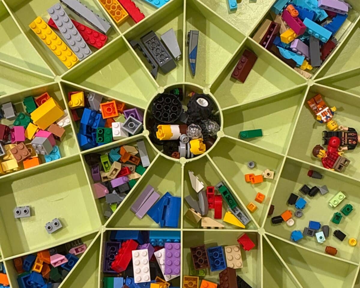 IKEA LEGO organizer. Top-down view of a circular LEGO sorting case with multiple segmented compartments filled with colorful bricks and a central cluster of black pieces.