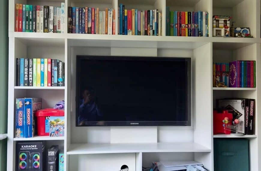 IKEA KALLAX LAPPLAND IKEA KALLAX LAPPLAND playroom storage and TV combo hack. white modular shelving unit filled with colorful books surrounding a mounted TV and small toy/set pieces on the right shelf area.