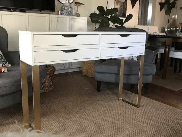 White four-drawer console table with gold metal legs in a living room setting.