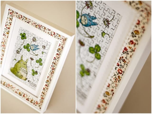 Framed decorative puzzle art with a white border and floral border, featuring whimsical cartoon characters, viewed at an angle.