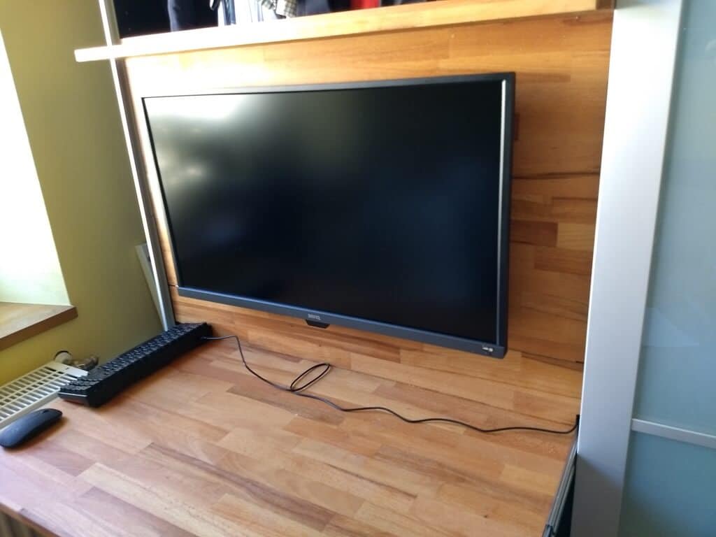 screen_open - IKEA Hackers Flat-screen TV mounted on a wooden wall panel with a keyboard and mouse on the desk in front.