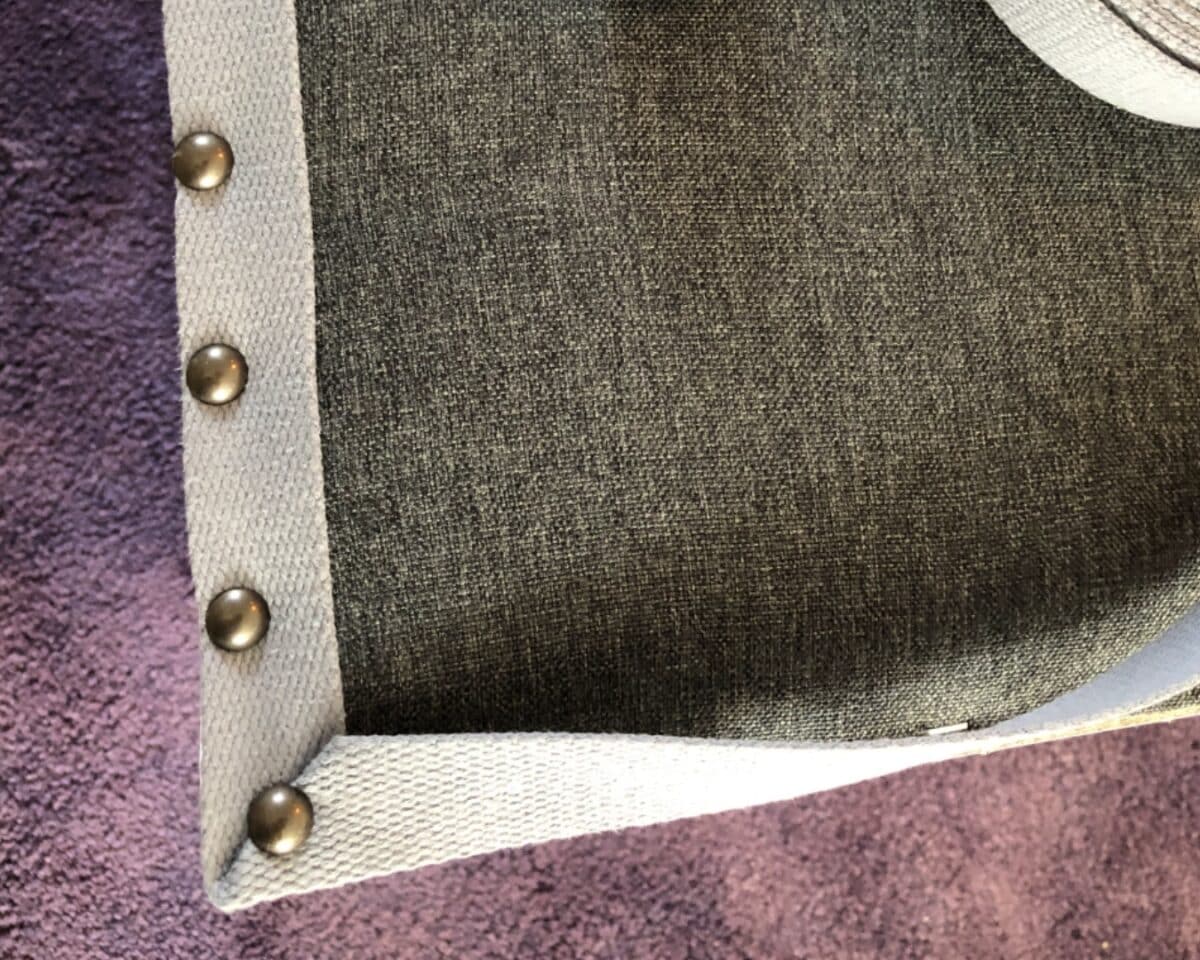 Close-up of light gray fabric with metal snap buttons along a purple plush surface, showing a curved edge.