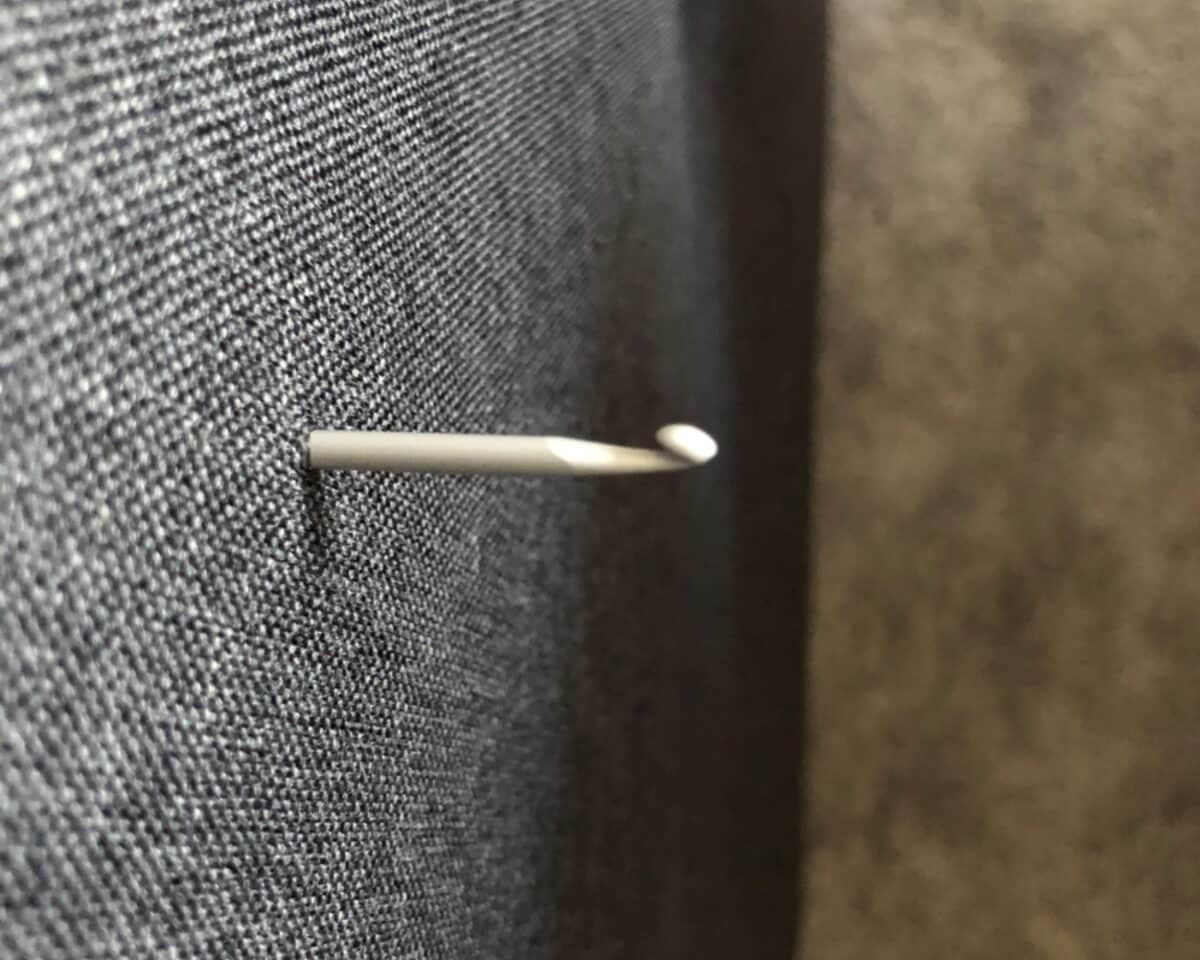 White sewing pin pierced through dark denim fabric, viewed from the side