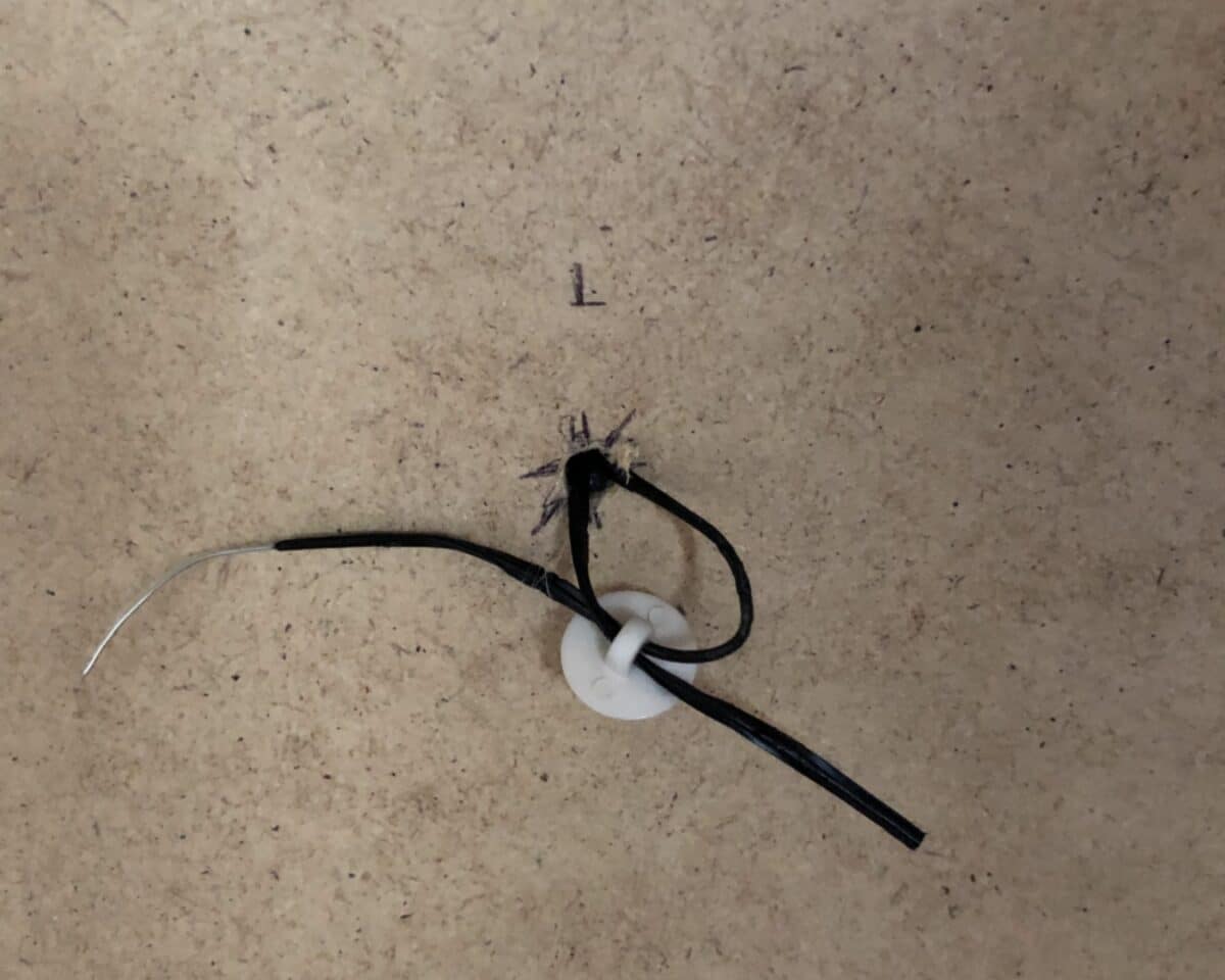 Damaged black electrical cord with exposed conductor and frayed insulation on a brown surface.