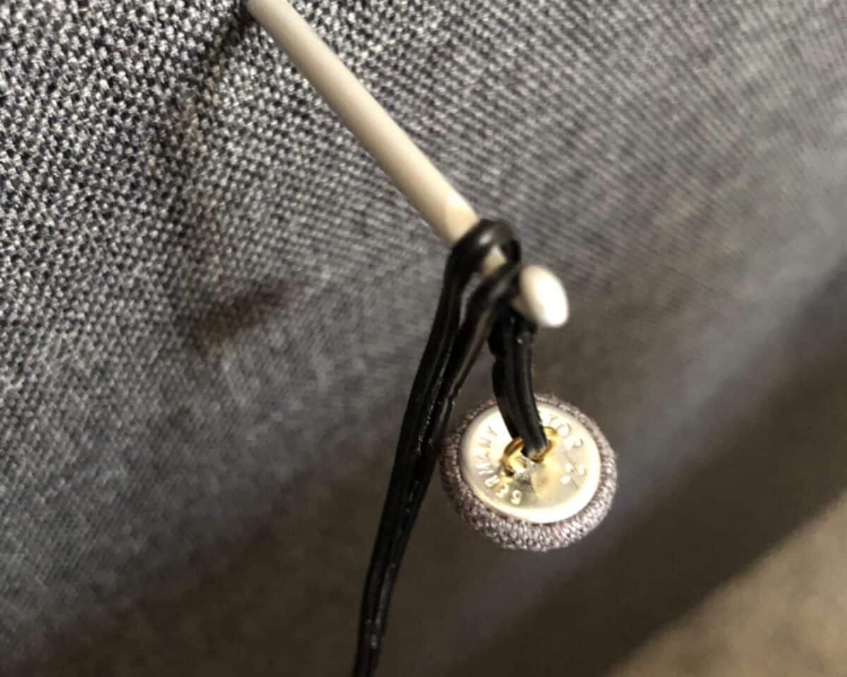 Close-up of a gray knit fabric with a small round metal snap and black drawstrings threaded through it.