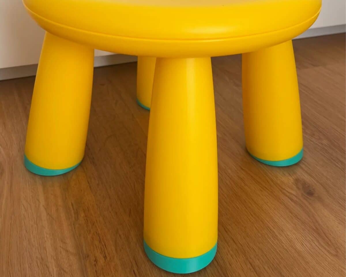 Yellow plastic IKEA MAMMUT stool with turquoise trim on a wooden floor.