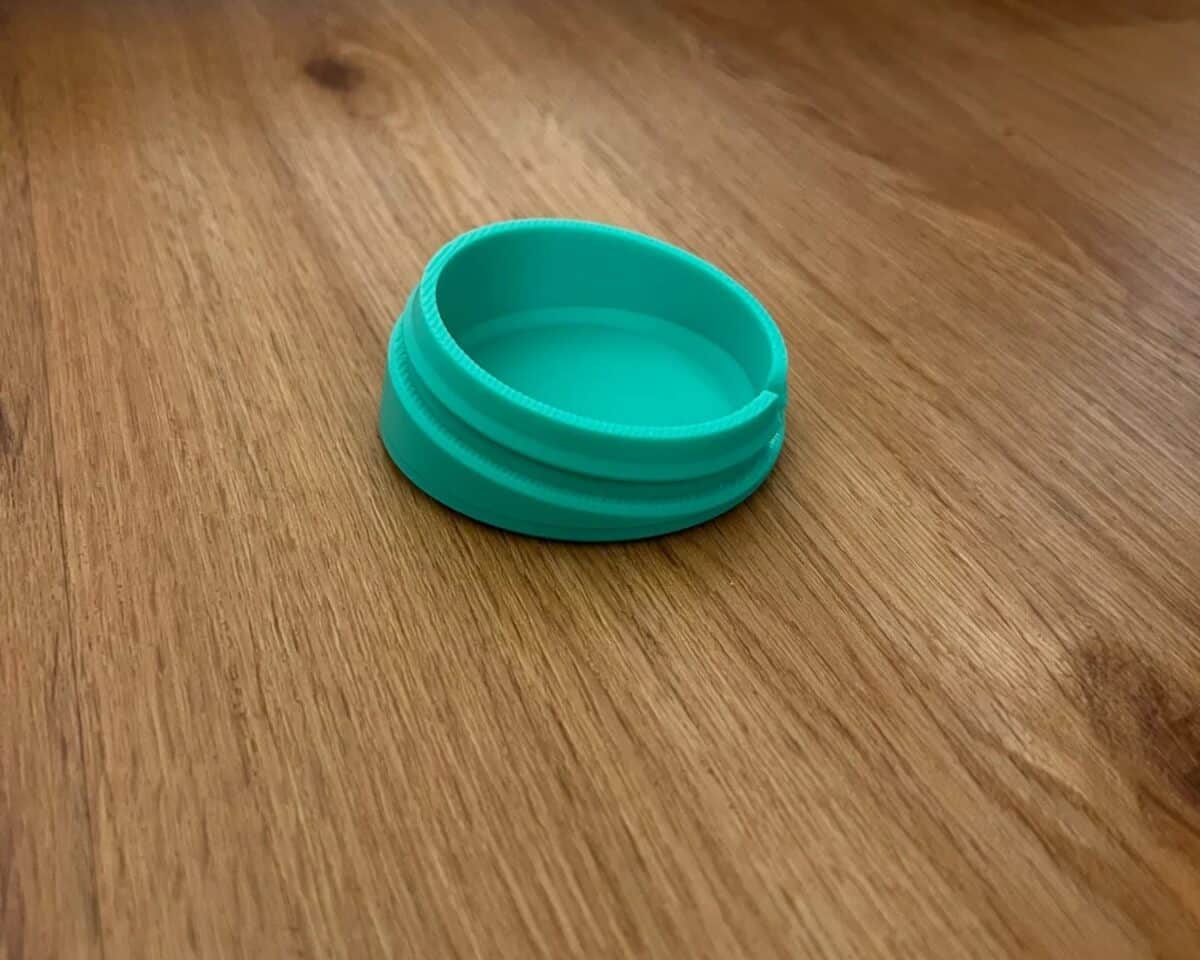 Teal round MAMMUT stool foot insert resting on a wooden table surface showing the grooves to be inserted into the stool