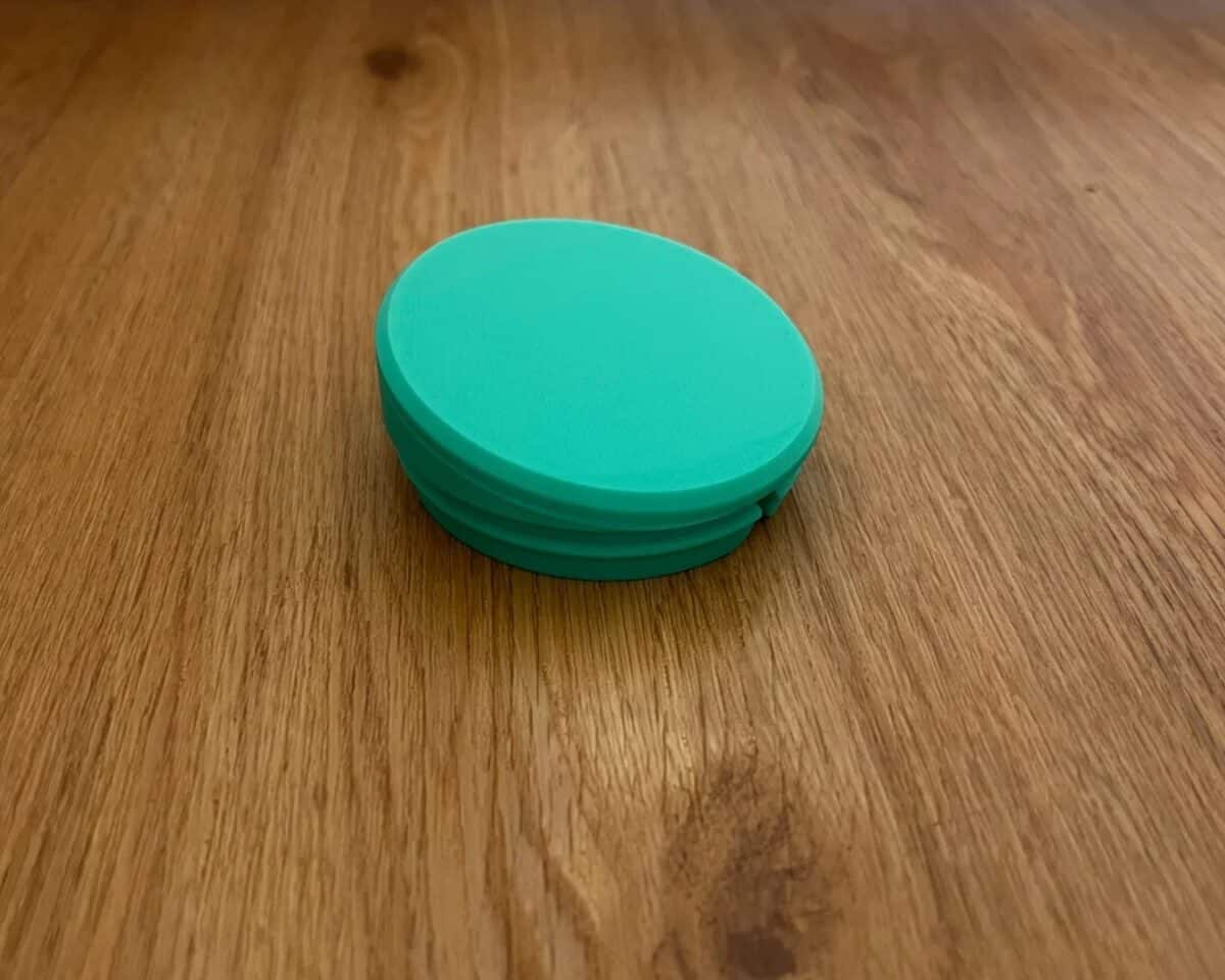 Teal round MAMMUT stool foot insert (silicone/plastic) on a wooden table, showing the base, floor side.
