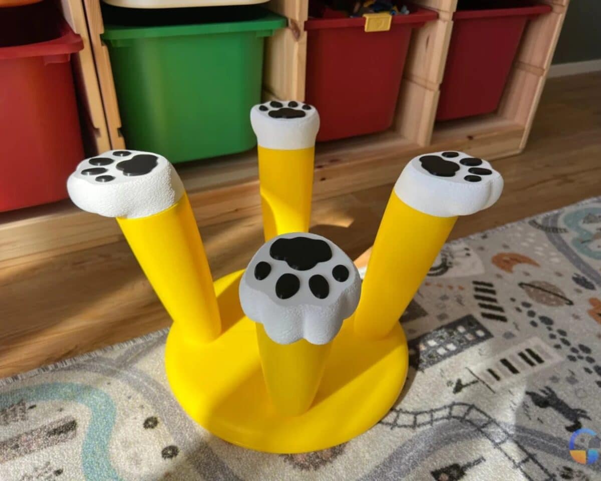 Bright yellow IKEA MAMMUT stool inverted with white paw-print caps on each leg, set on a patterned rug in a child’s playroom next to storage bins.