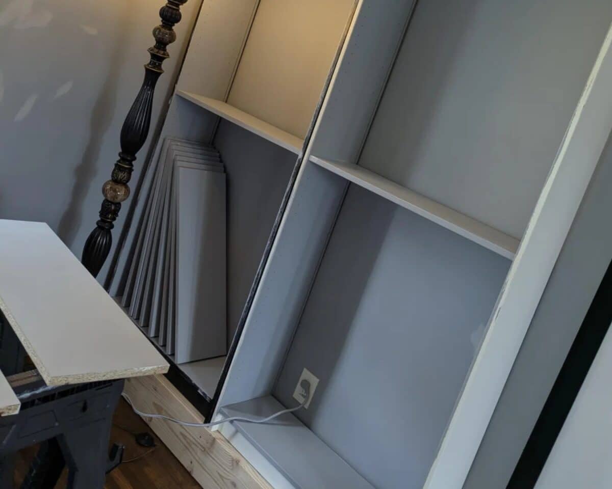 Workshop scene with gray built shelves, leaning boards, and a tall carved lamp post nearby.