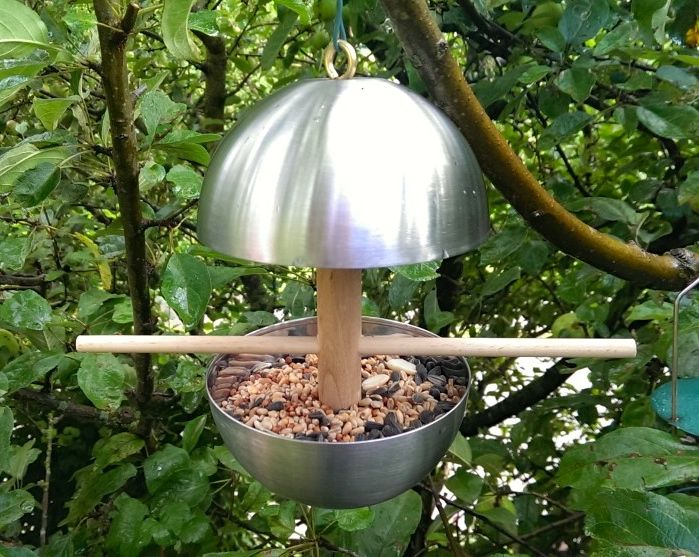 birdfeedercrop - IKEA Hackers Shiny metal-domed bird feeder with a seed-filled basin and a wooden center post.