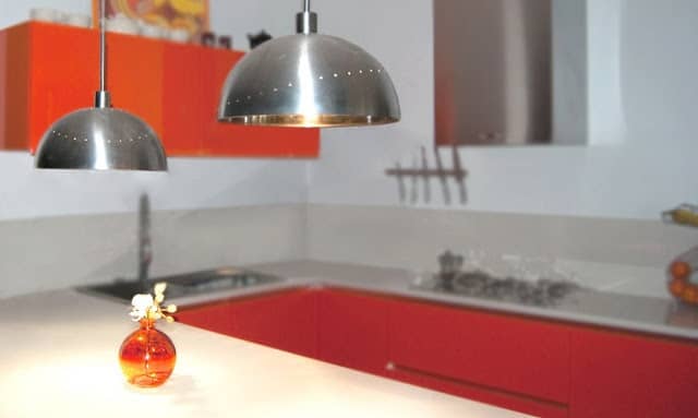 lampade-2-784291 - IKEA Hackers Modern kitchen with red lower cabinets, stainless steel pendant lights, and a small orange glass vase with white flowers on a white countertop.