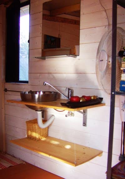 rsz_1manuele_foto_795-798284 - IKEA Hackers Compact wooden kitchenette: stainless sink with curved faucet on a wall-mounted shelf, lower wicker basket beneath, tray of peppers on the counter, mirror cabinet above, standing fan to the right, window to the left.