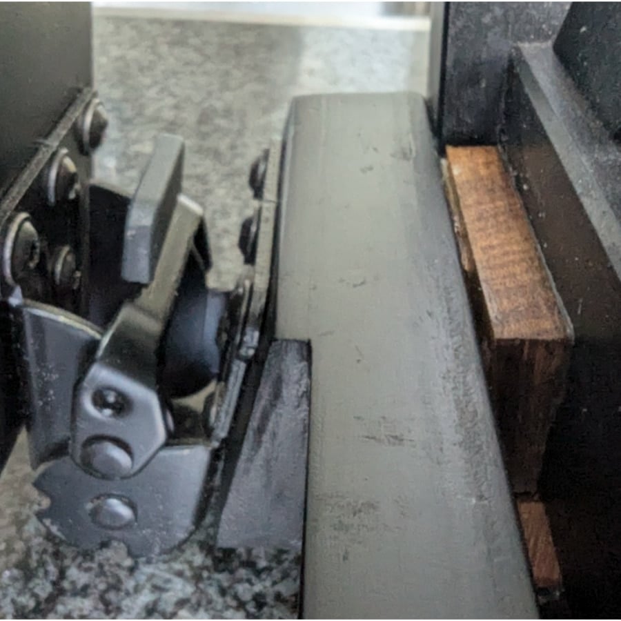 23 - IKEA Hackers Close-up of a gray metal clamp/hinge attached to a dark surface, with a wooden block nearby on a speckled countertop.