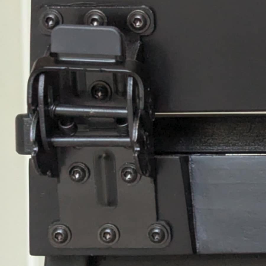 26 - IKEA Hackers Close-up of a black metal hinge assembly with exposed pins and multiple screws on a machine panel.