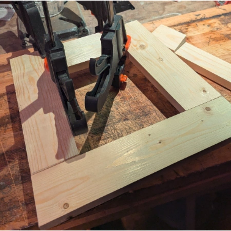 30 - IKEA Hackers Bar clamps hold together light pine boards forming a rectangular frame on a workbench.