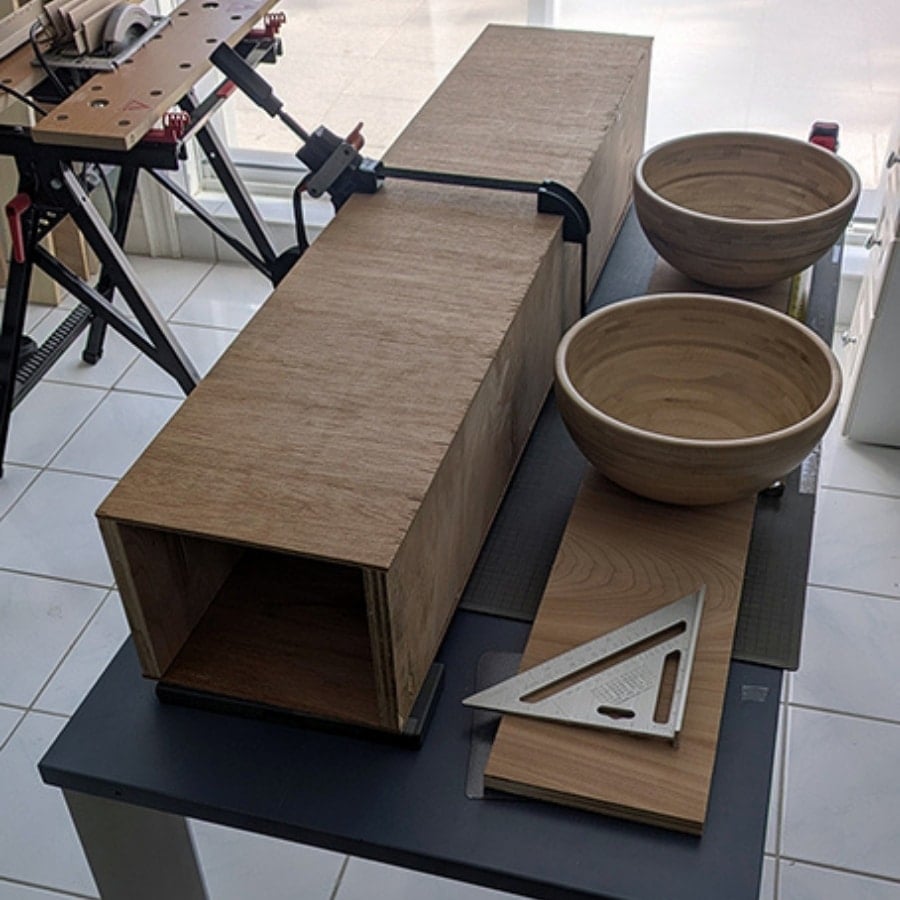 39 - IKEA Hackers Woodworking bench with a rectangular cabinet box, two wooden bowls, clamps, and a triangle ruler on a worktable