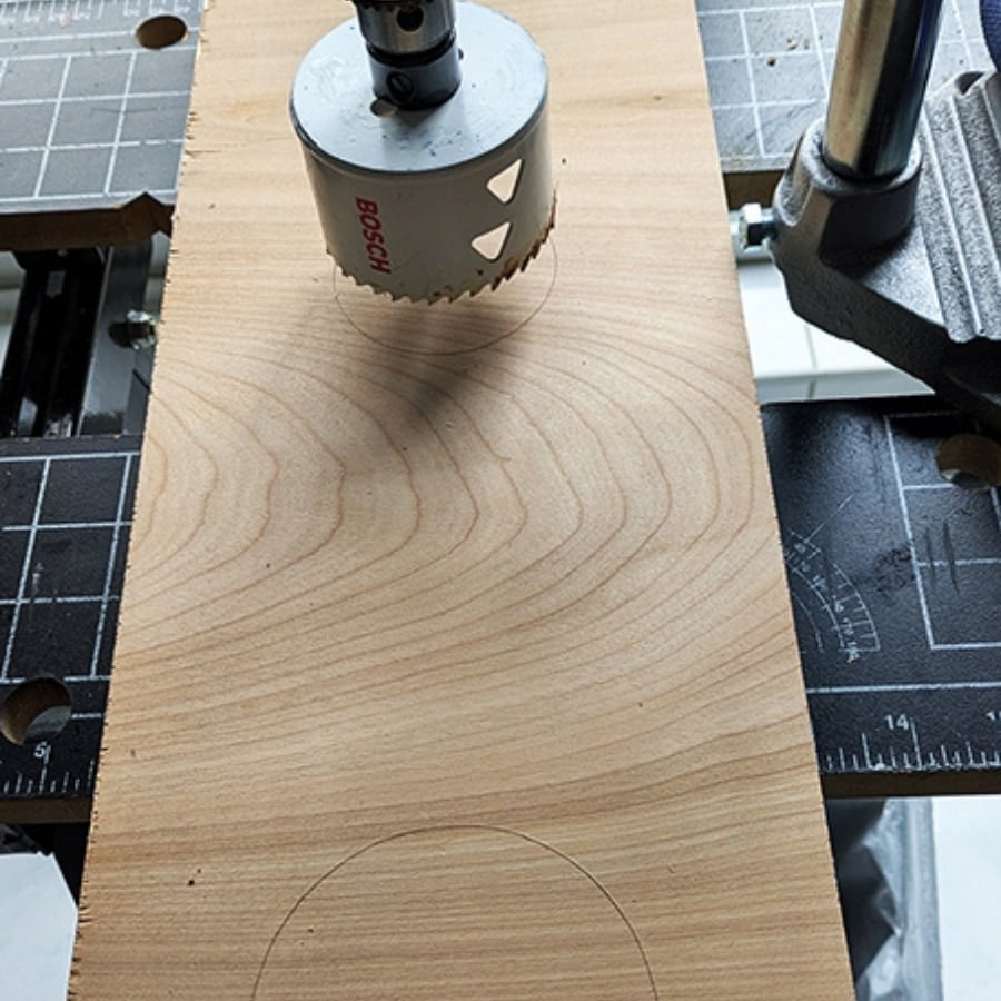 42 - IKEA Hackers Bosch hole saw attached to a drill press cutting a circular pattern into a plywood plank.