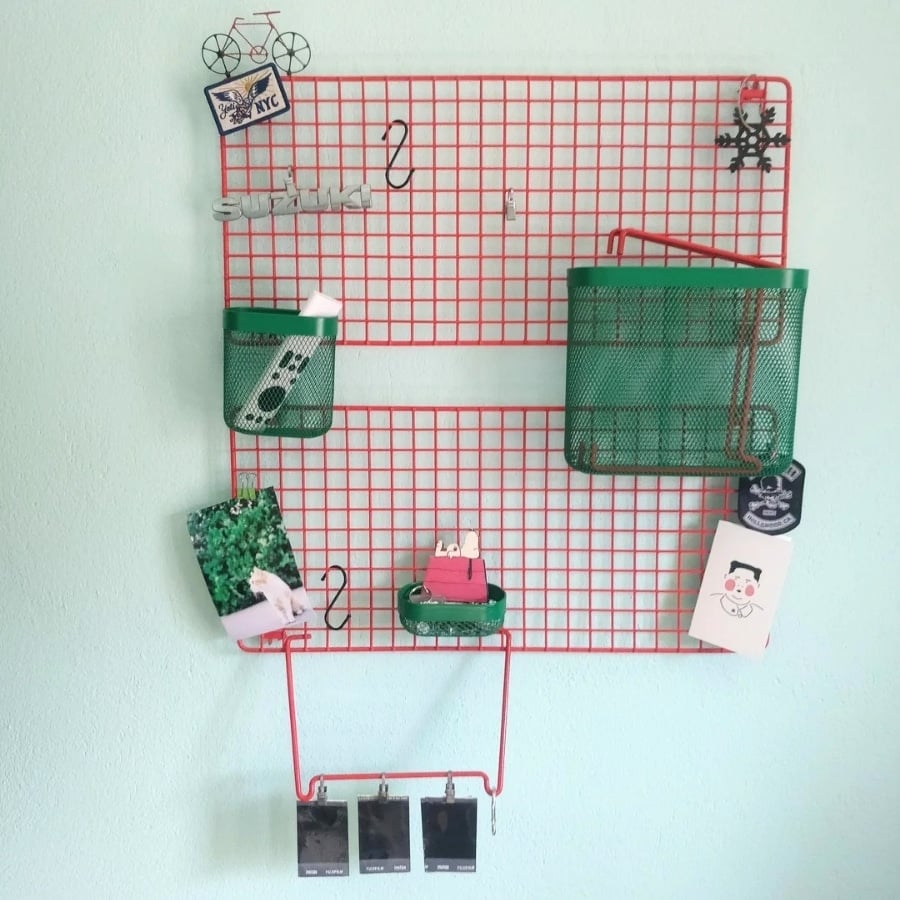 IKEA GREJIG shoe rack hack. Red wire grid wall organizer with two green baskets holding desk items and photos, mounted on a light blue wall.